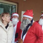 Stanovalka doma za starejše se pogovarja z obiskovalci, oblečenimi v Božičke, pred vhodom v stavbo.