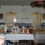 Duhovnik daruje božično sveto mašo za stanovalce v jedilnici doma, oltar je okrašen z adventnimi svečami in jaslicami.