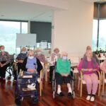 Skupina stanovalcev sedi v prvih vrstah in spremlja božično bogoslužje, nekateri uporabljajo pripomočke za hojo.