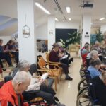 Stanovalci doma za starejše sedijo v polkrogu v večnamenskem prostoru in spremljajo božično tombolo.