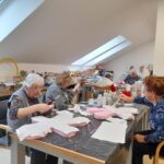 Stanovalke za mizo ustvarjajo okraske iz stiropora in papirja ter jih premazujejo z lepilom v ustvarjalni delavnici.