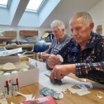 Stanovalca pri mizi izrezujeta papirnate motive in pripravljata okraske v okviru ustvarjalne delavnice.