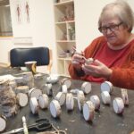 Stanovalka sedi za mizo in z natančnostjo barva majhne lesene kolute, pripravljene za praznično okrasitev.