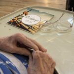 Na mizi ležijo očala in koledar za leto 2026, v ospredju so vidne roke starejše osebe.