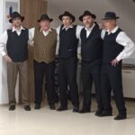 Pet članov folklorne skupine v tradicionalnih oblačilih stoji skupaj in pozira v notranjem prostoru doma starejših.