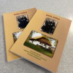 Dve izvodni knjigi z naslovom »Naša hiška«, na naslovnici pa stara fotografija para in slika tradicionalne hiše; knjigi sta odloženi na svetli površini.