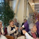 Miklavž deli darila stanovalcem doma, ki sedijo okoli mize v skupnem prostoru.