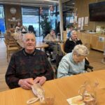 Stanovalci doma sedijo v skupnem prostoru in prejemajo miklavževa darila.