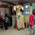 Miklavž z spremstvom hodi po hodniku med sedečimi stanovalci doma in jim deli darila.