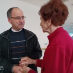 Odrasel moški se pogovarja s stanovalko in ji prijazno drži roko v svetlem skupnem prostoru.