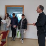 Birmanci stojijo v vrsti in berejo besedilo z listov, ob njih stoji odrasel moški, ki jih posluša.