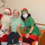 Božiček in palčica podarjata darilo nasmejani stanovalki.