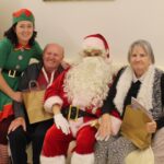 Božiček in palčica s stanovalcema, ki držita darilne vrečke.