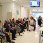 Sv. Miklavž pozdravlja skupino stanovalcev, ki sedijo v vrsti na hodniku doma za starejše.