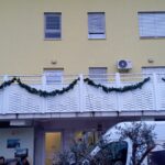 Zunanja stran doma okrašena z dolgimi zelenimi girlandami, obešenimi vzdolž balkona.