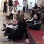 Otroci in odrasli so zbrani v prostoru doma; otroci stojijo v ospredju, v ozadju sedijo stanovalci in spremljajo dogajanje.