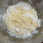 Testo za potico v kovinski skledi, delno posuto z moko med mešanjem.