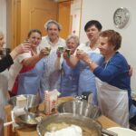 Skupina stanovalk in zaposlenih v predpasnikih nazdravlja s papirnatimi kozarci po končani pripravi potice.