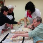 Stanovalke in spremljevalka polagajo izrezane piškote na pekač, obložen s papirjem za peko, med skupno peko božičnih keksov.