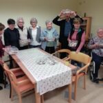 Skupina starejših stanovalcev pozira v prostoru in drži posode z pripravljenimi božičnimi keksi po zaključeni peki.