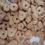 Velika količina doma pripravljenih piškotov različnih oblik (srčki, rožice, zvezdice) razporejenih po pladnju; v ospredju je vidna roka osebe, ki jih razporeja.