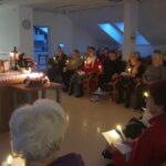 Duhovnik daruje polnočno mašo v prostoru doma, stanovalci sedijo v polkrogu in v rokah držijo prižgane sveče.