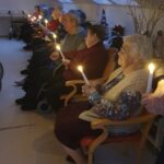 Stanovalke in stanovalci, sedeči v vrstah, pri polnočni maši držijo prižgane sveče in sledijo bogoslužju.