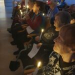 Stanovalke in stanovalci z zbranimi obrazi berejo besedila in držijo prižgane sveče med polnočno mašo.