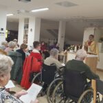 Pogled na zbrane stanovalce v invalidskih vozičkih in na stolih, ki spremljajo polnočno mašo v domu.