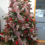 Veliko božično drevo v notranjem prostoru, bogato okrašeno z rdečimi in belimi trakovi, okraski in lučkami.