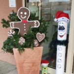 Praznična božična dekoracija pred vhodom v stavbo, z okrašenim zelenjem, medenjakovimi motivi in snežakom.