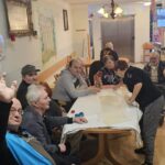 Stanovalci sedijo ob mizi in sodelujejo pri pripravi prazničnega peciva v skupnem prostoru doma.