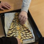 Roke polagajo pečeno praznično pecivo v obliki smrečice na pekač, pripravljen za postrežbo.