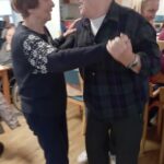 Stanovalka in stanovalec plešeta v skupnem prostoru doma, ob njiju stoji spremljevalka.