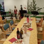 Praznično pogrnjena dolga miza z dobrotami, steklenicami in božično dekoracijo v skupnem prostoru.