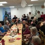 Stanovalci sedijo ob praznično pogrnjeni mizi in se družijo v okrašenem prostoru.