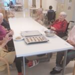 Stanovalci sedijo za mizo in oblikujejo testo za piškote, pripravljene kroglice so zložene na pekaču.