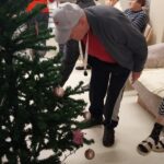 Stanovalci sodelujejo pri okraševanju novoletne smrečice, drugi sedijo in opazujejo dogajanje v prostoru.