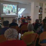 Stanovalci doma za starejše sedijo v skupnem prostoru in gledajo film, ki je predvajan na projekcijskem platnu.