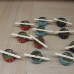 Sveže izdelane naravne sveče v barvitih posodicah, ki se hladijo z lesenimi paličicami za stabilizacijo stenja.