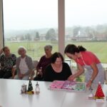 Skupina stanovalcev opazuje predstavitev izdelave mil, pred njimi so pripravljene posode, kalupi in sestavine.