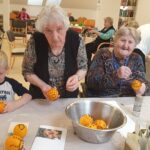 Otrok in stanovalke doma za starejše skupaj okrašujejo pomaranče s klinčki med ustvarjalno delavnico.