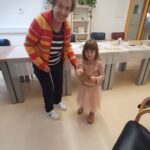 Stanovalka in deklica se držita za roke ter ponosno kažeta izdelek, narejen na ustvarjalni delavnici.