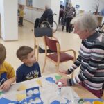 Stanovalka doma za starejše klepeta z dvema dečkoma, ki ustvarjata praznične okraske.