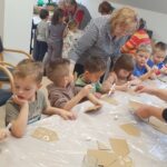 Otroci v vrtcu ustvarjajo na delavnici, kjer jim pri delu pomagajo stanovalke doma za starejše.