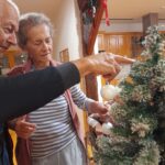 Stanovalca skupaj nameščata božične okraske na okrašeno zeleno vejo v skupnem prostoru.