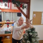 Stanovalec namešča zvezdo na vrh božičnega drevesca v skupnem prostoru doma.