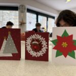 Tri ročno izdelane praznične voščilnice z motivi božičnega drevesca, venčka z jelenčkom in božične zvezde so razstavljene na mizi.