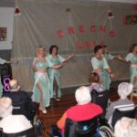 Plesna skupina nastopa pred stanovalci doma starejših na praznični prireditvi ob zaključku leta.