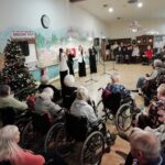 Nastop pevskega kvarteta pred številnim občinstvom stanovalcev v invalidskih vozičkih v praznično okrašeni dvorani.